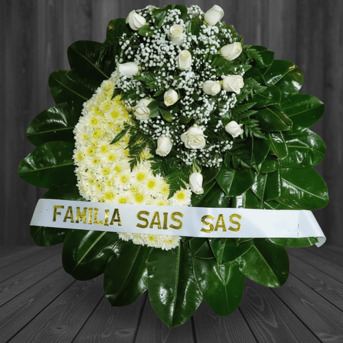 arreglo fúnebre redondo con flores blancas y follaje verde oscuro sobre fondo de madera gris, con cinta blanca que dice familia sais sas
