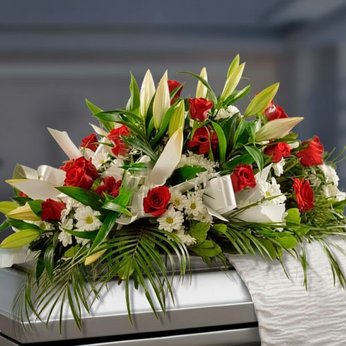 Arreglo de flores sobre un ataúd con lirios blancos, rosas rojas, margaritas blancas y follaje verde
