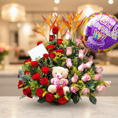 Arreglo de flores con rosas rojas y rosas, flores exóticas naranjas, peluche de oso y globo de feliz cumpleaños sobre mesa en interior