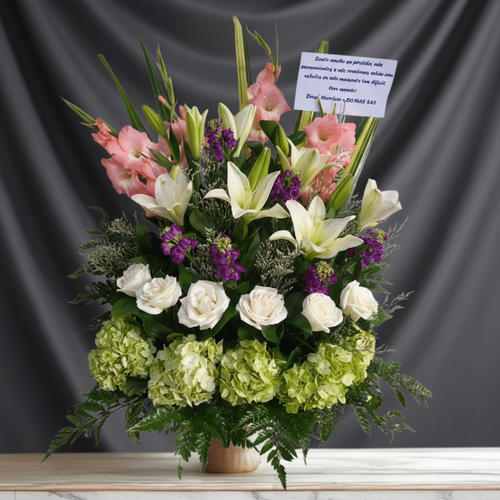 Arreglo floral grande con rosas blancas, lirios blancos, hortensias verdes, flores rosadas y moradas, con tarjeta de condolencias sobre fondo gris