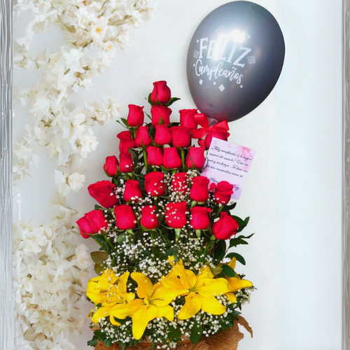 Arreglo de flores con varias filas de rosas rojas, lirios amarillos en la base, follaje verde, nube blanca decorativa y globo negro con texto Feliz Cumpleaños