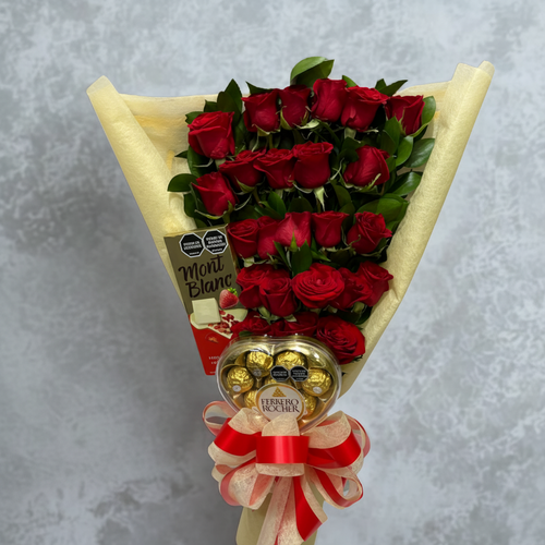 Arreglo de ramo envuelto en papel crema con rosas rojas en varias filas, chocolates Ferrero Rocher en la base y barra de chocolate Mont Blanc al lado, decorado con moño rojo y crema sobre fondo gris marmoleado
