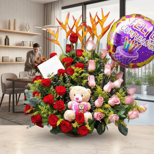 Arreglo floral de rosas rojas y rosas con aves del paraíso, globo de feliz cumpleaños y oso de peluche sobre mesa en sala comedor moderna con hombre al fondo preparando la mesa