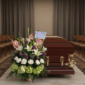 Arreglo de flores fúnebres con lirios blancos, rosas y claveles junto a un ataúd de madera barnizada con herrajes dorados en una sala velatoria